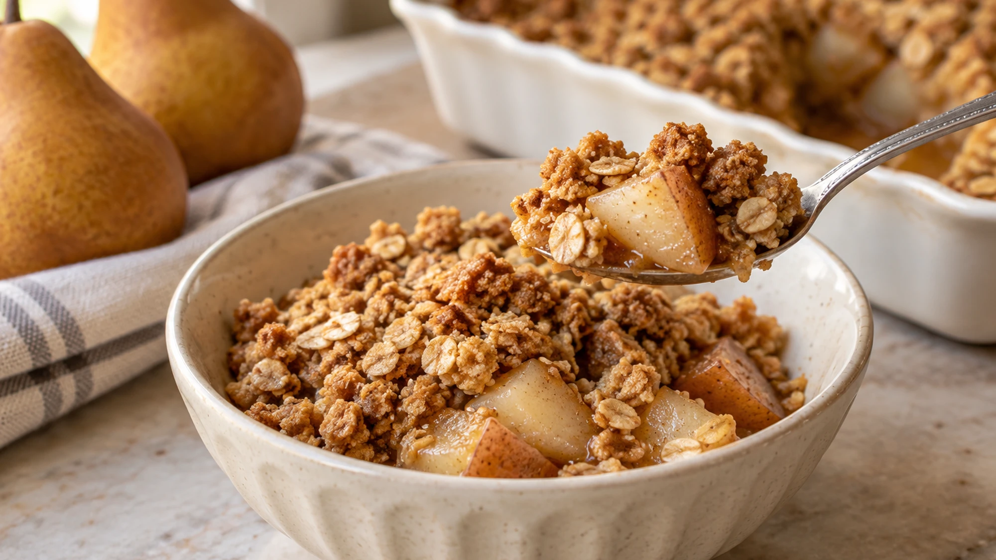 A spoonful of pear crisp lifted above a bowl with tender fruit and oat topping